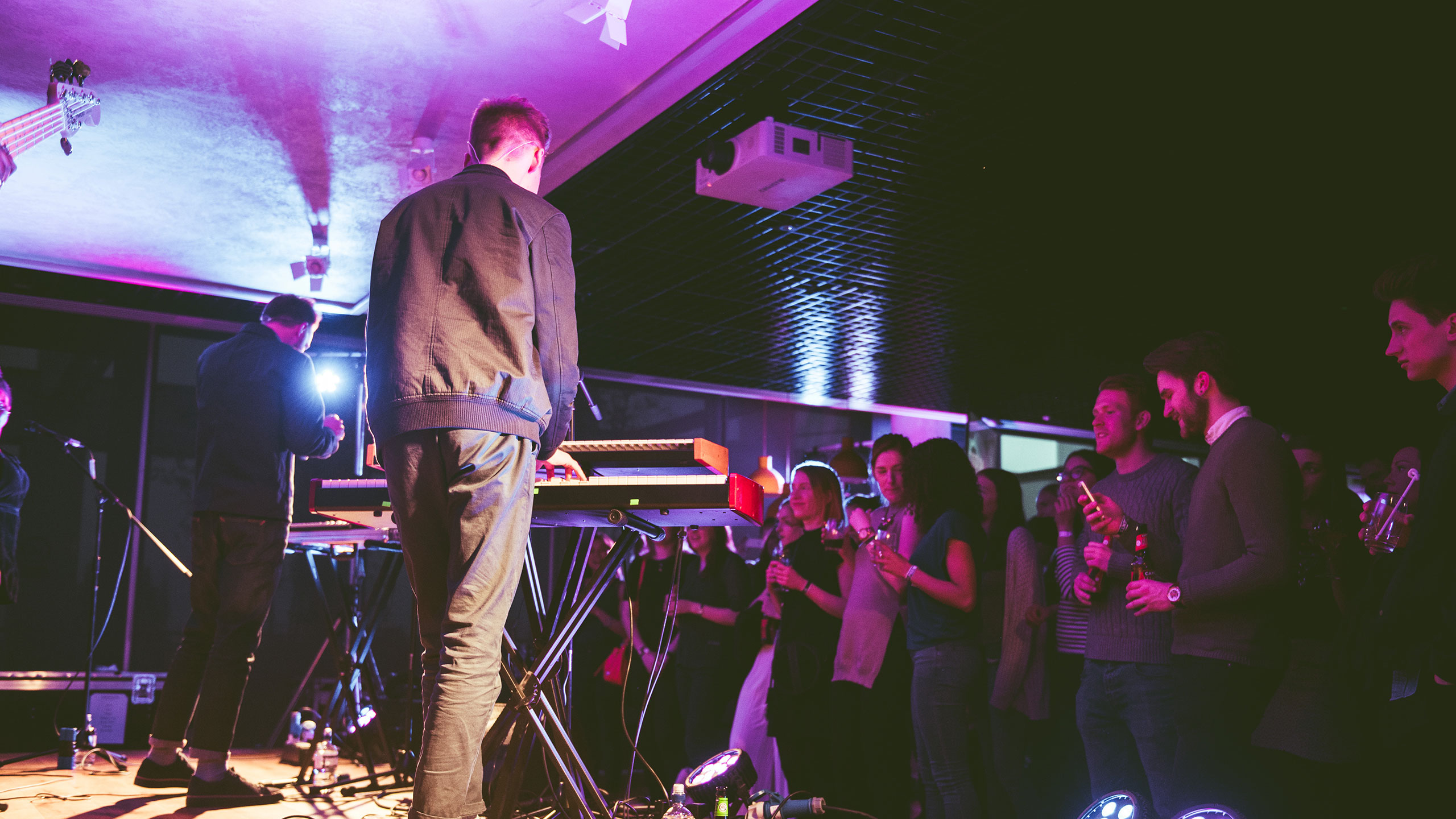 A shot from behind Honne performing keyboards and singing on stage at PRS Presents, the audience are chatting