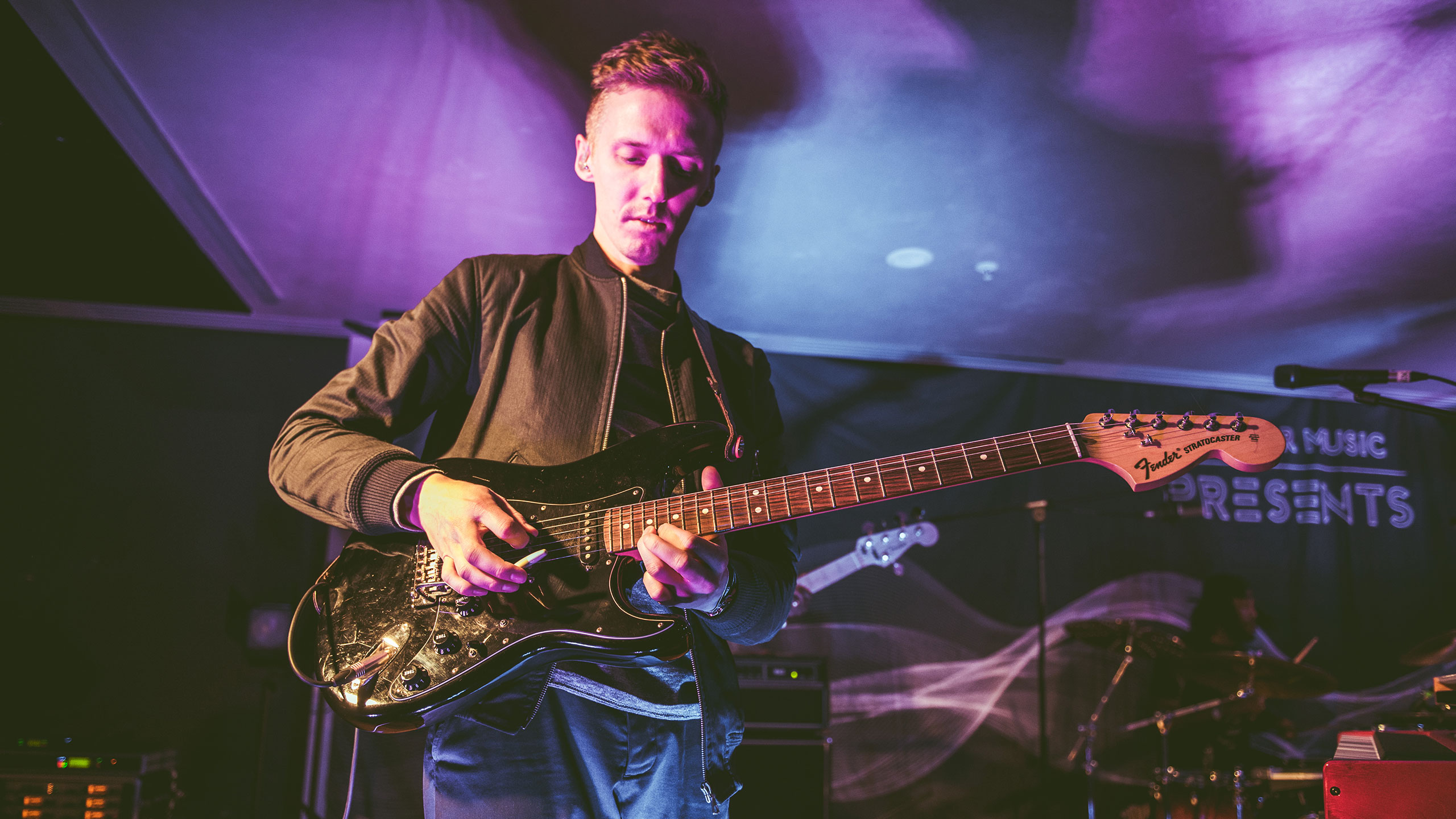 Honne's James Hatcher plays a black guitar on stage at PRS Presents, wearing a dark shirt
