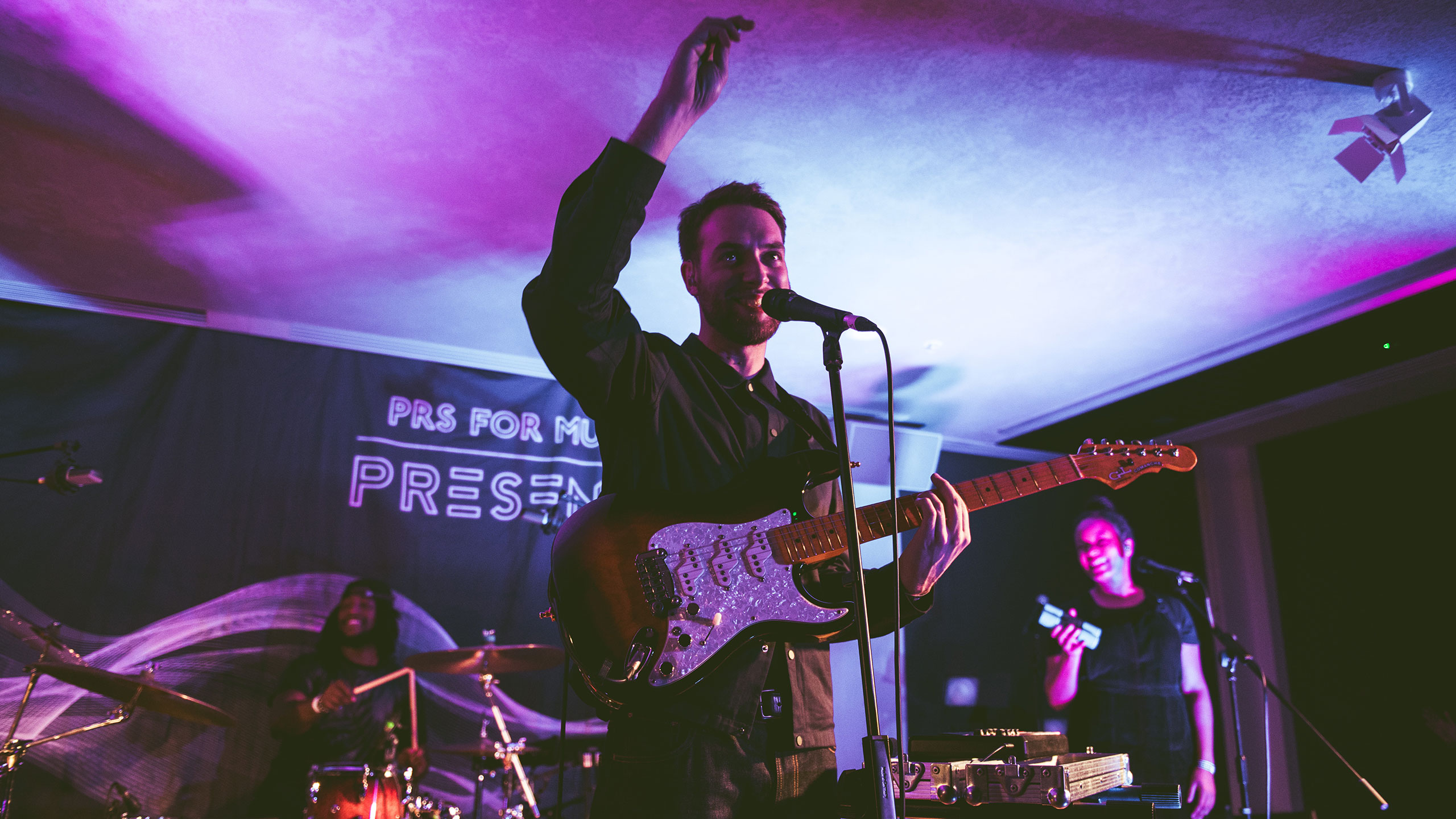 Honne's Andy Clutterbuck raises his arm as he sings and plays guitar at PRS Presents