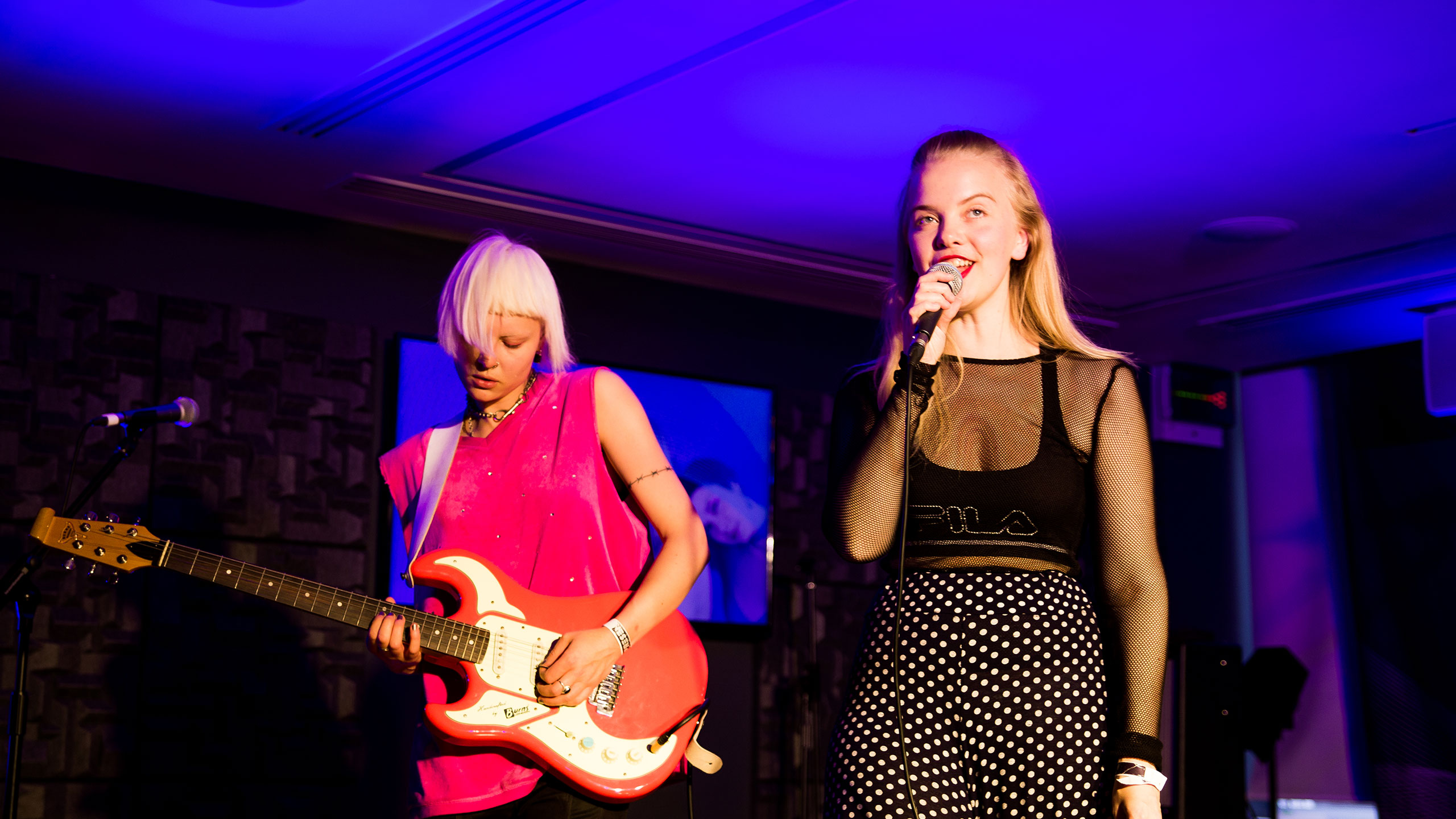 Dream Wife's Rakel Mjoll, wearing a black outfit, sings and Alice Go, wearing a bright pink top, plays guitar on stage at PRS for music Presents