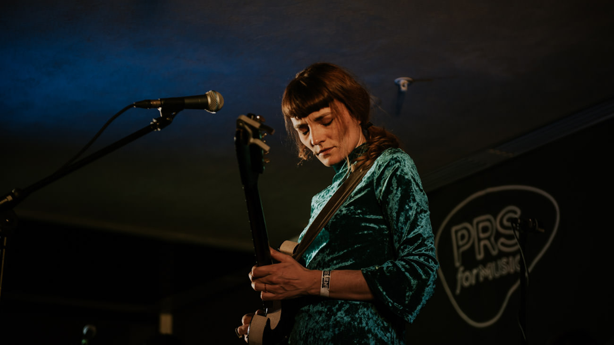 Halo Maud, wearing a green velvet dress, playing guitar on stage at PRS for Music Presents