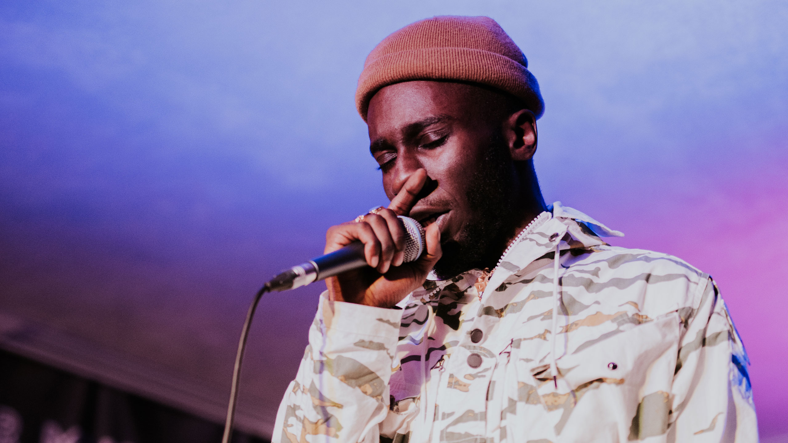 Kojey Radical in a beanie hat and camouflage jacket singing at PRS for Music Present