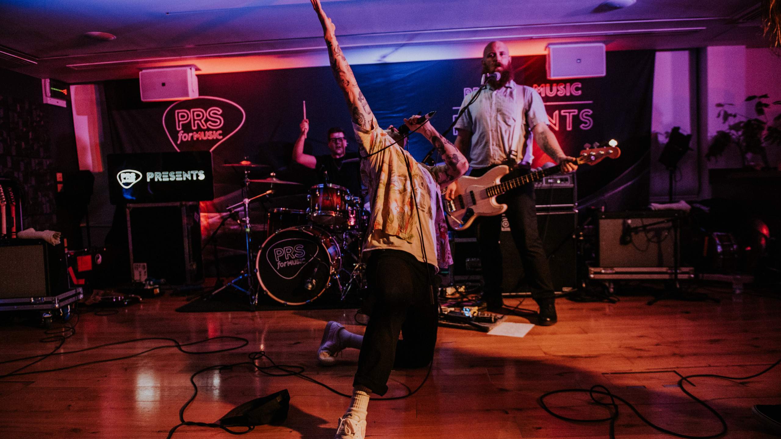 Idles frontman Joe Talbot kneels and raises his arm on stage at PRS for Music Presents